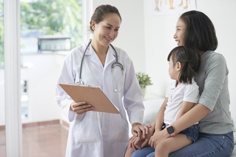 Female pediatrician reassuring mother of little Asian girl